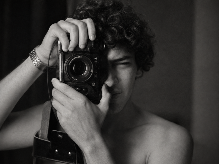Joven con cabello rizado tomando una foto con cámara en blanco y negro.