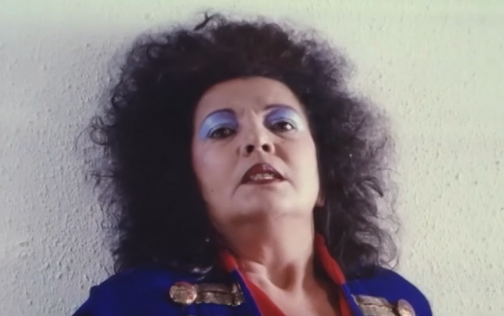 Retrato de una mujer con maquillaje llamativo y cabello rizado en un fondo neutro.