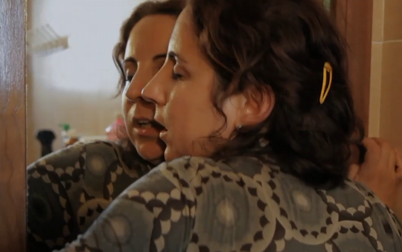 Mujeres abrazadas frente a un espejo en un ambiente cálido y acogedor.